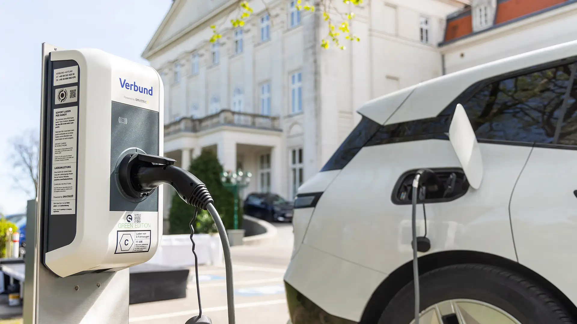 Ein E-Auto wird an einer VERBUND Ladestation auf dem Parkplatz eines Hotels geladen.